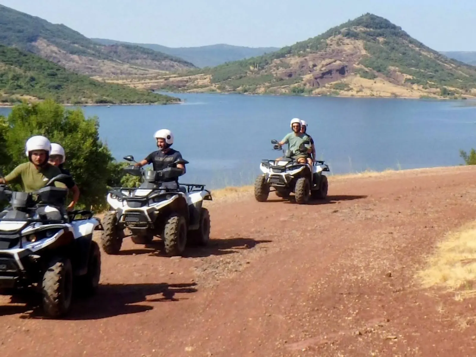 Quads en file sur une piste de terre rouge au bord du lac du Salagou