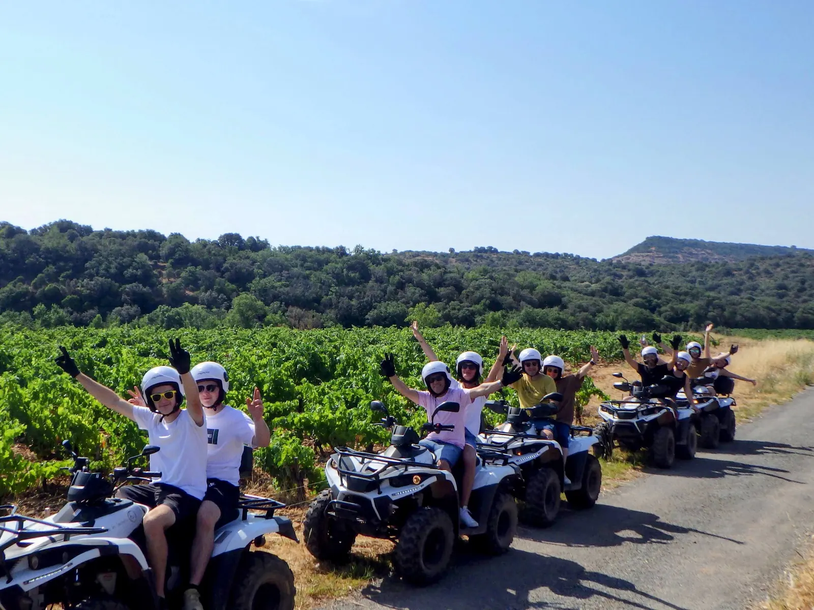Groupe de randonneurs en quad, bras levés, le long des vignes