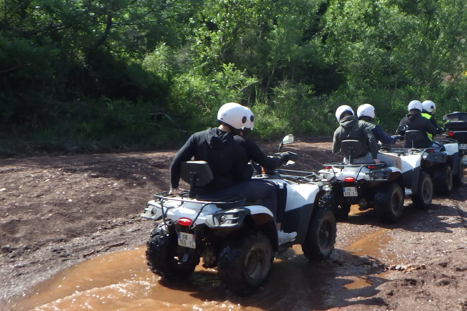 Quads en file traversant un passage d'eau sur un chemin de terre rouge