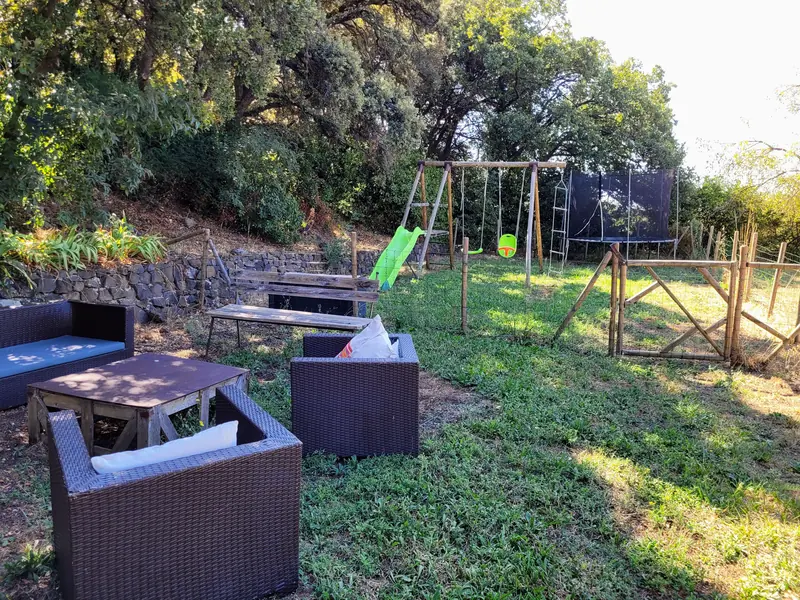 Salon de jardin et aire de jeux avec balançoire et trampoline dans le jardin du gîte