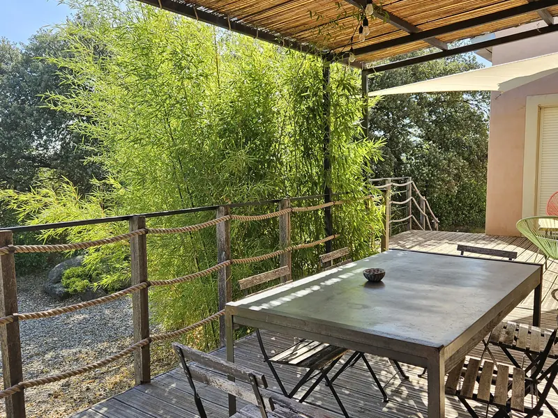 Terrasse couverte du gîte, avec sa table sous la pergola et le bambou